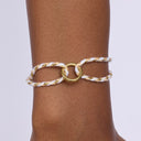 Gold and white braided anklet on a person's ankle against a light purple background